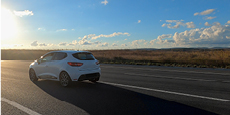 White car driving on road against blue sky on sunny day.